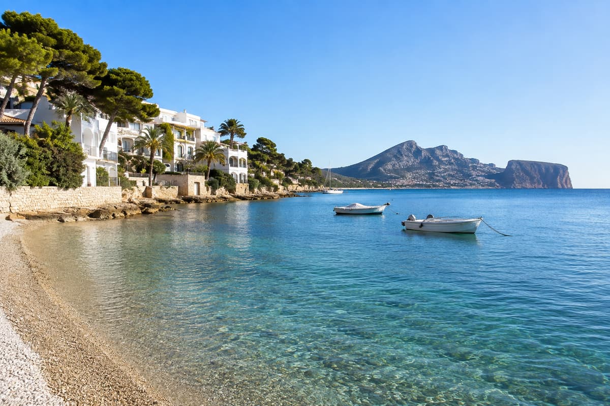 Cala de la costa de Altea con barcas fondeadas y edificios de apartamentos entre pinos